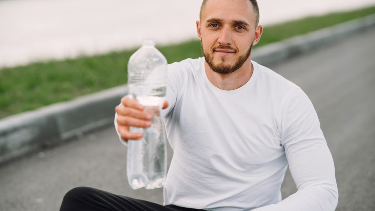 Athletic man with bottled water sitting outdoors, promoting hydration.