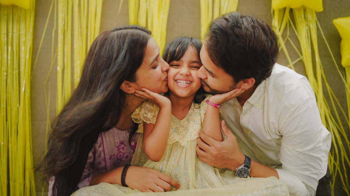 A heartwarming family moment with parents kissing their daughter during a festive celebration.